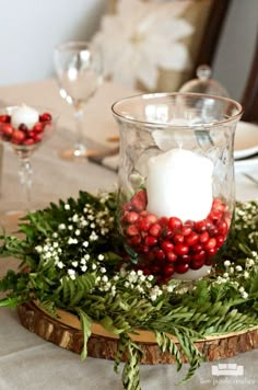 a candle is sitting in a glass bowl on a table with greenery and berries