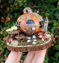 a hand holding a miniature fairy house made out of wood and moss with mushrooms on it