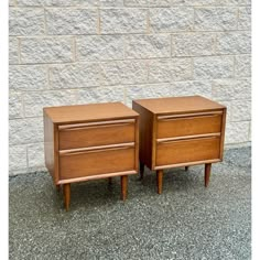 two wooden nightstands sitting next to each other in front of a white brick wall