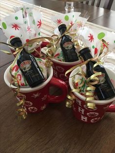 three coffee mugs filled with liquor bottles wrapped in gold ribbon and bows, sitting on top of a wooden table