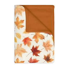 an orange and white blanket with autumn leaves on the bottom, in front of a white background