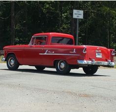 an old red truck is parked on the side of the road in front of some trees