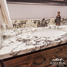 a bathroom sink with marble counter top and wooden drawers