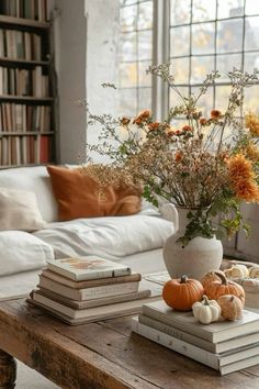 a coffee table with books and flowers on it in front of a window filled with books