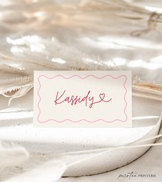 a white table with a pink name tag sitting on it's side next to feathers