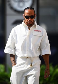 a man in white suit and sunglasses walking down the street with his hand on his hip