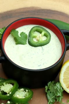 a red bowl filled with white sauce next to sliced green peppers and lemon wedges