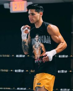 a man standing next to a boxing ring wearing yellow shorts and a black tank top