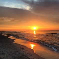 the sun is setting over the ocean with people in the water and on the beach