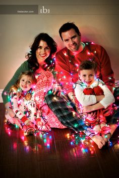 a family sitting on the floor in front of christmas lights with their arms around each other