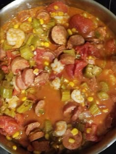 a pan full of food sitting on top of a stove next to a pot filled with hotdogs and corn