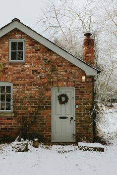 a small brick house with a wreath on the front door and windows in the snow