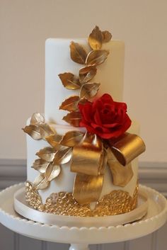 a white and gold wedding cake with a red rose on top