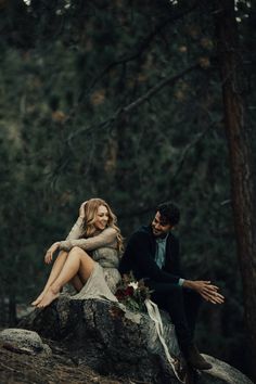 a man and woman sitting on top of a rock in the woods