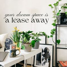 a living room filled with lots of plants next to a white table topped with pictures