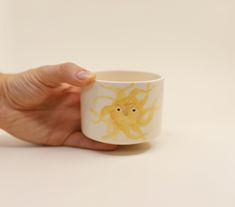 a hand holding a coffee cup with an image of a yellow octopus on it's side