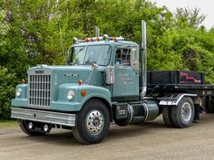 a green semi truck parked in front of some trees