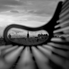 a black and white photo of a park bench in front of a cityscape