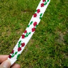 a hand holding a white and red string with flowers on it in the grass next to a green field