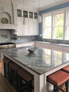 a large kitchen with marble counter tops and stools in front of an island that is surrounded by white cabinets