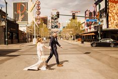 a bride and groom crossing the street in front of neon signs at their las vegas wedding