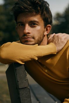 a man leaning on a wooden bench with his hand on his shoulder and looking at the camera