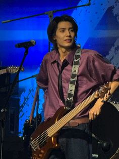 a man holding a guitar while standing in front of a microphone