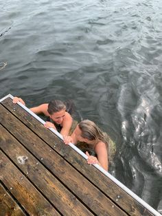 two women are in the water looking out from a dock at some birds flying over them