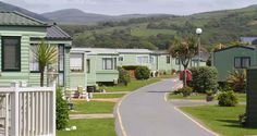 a street lined with green homes on both sides of the road and hills in the background