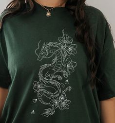 Be a trend-setter in our River Dragon Tee! Flaunt your bad-ass attitude with the cool dragon print, while still maintaining comfort with the 100% cotton, relaxed fit. You're no princess, you're a dragon ready to take on the streets. 🐉 Ain't no one gonna stop you! This is a unisex tee so check the size guide for measurements! and if you want to rock that oversized look go up a few sizes. This product is made especially for you as soon as you place an order, which is why it takes us a bit longer Casual Cotton Tops With Dragon Design, Casual Cotton Top With Dragon Design, Casual Dragon Design Tops For Streetwear, Casual Tops With Dragon Design For Streetwear, Dragon Shirt Design, Graphic Design T Shirt, River Dragon, Short Sleeve Tops With Dragon Print For Streetwear, Dragon Tshirt Design