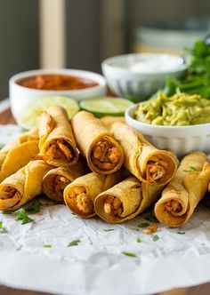 several burritos on a table with guacamole and salsa in the background