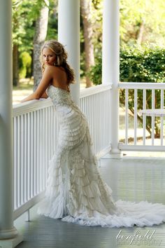 a woman in a wedding dress leaning on a white porch railing with her back to the camera