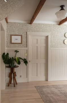 a room with white walls and wooden floors, two plants on the table in front of the door