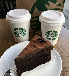 a slice of chocolate cake on a plate with two cups of starbucks coffee in the background