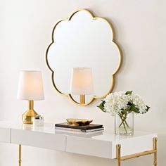 a white table with two lamps and a mirror on the wall above it, along with a vase filled with flowers