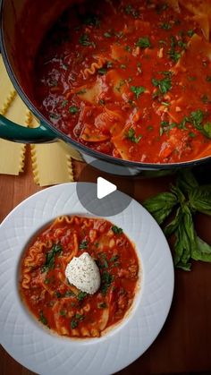 a pan filled with pasta and sauce on top of a wooden table next to a white plate