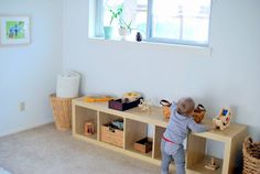 a toddler playing with toys on a wooden shelf in a white walled children's room