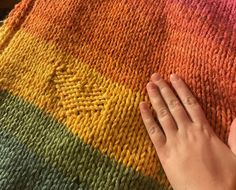 a person's hand resting on a multicolored knitted blanket with their fingers