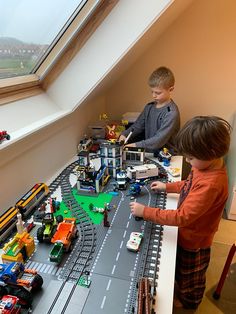 two boys are playing with toy trains and cars in the room on the windowsill