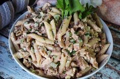 a white bowl filled with pasta and meat on top of a wooden table next to flowers