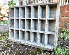 an old wooden shelf sitting on the ground in front of a brick wall and flower bed