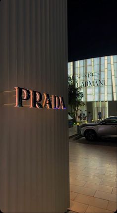 the word prada is lit up at night in front of a building with cars parked outside