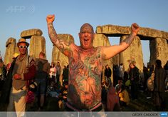 a man with tattoos on his body standing in front of stonehenge at sunset