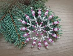 a snowflake ornament with pink and white beads on a wooden table