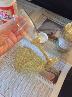 a person holding a wine glass with gold glitter on it next to a newspaper page