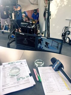 a table with papers and microphones on it, in front of a television screen