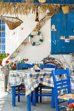 an outdoor dining area with blue chairs and table covered in plaid cloths, next to a thatched roof