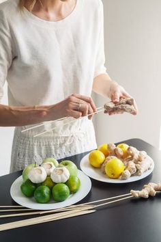 a woman preparing food with chopsticks and lemons on the table next to her