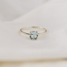 a white gold ring with an aqua blue topazte in the center on a white cloth