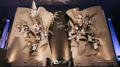 two floral arrangements are on display in front of a backdrop for the opening of an event